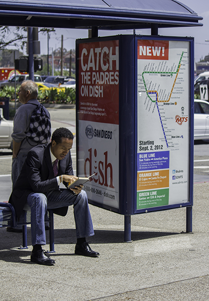 man reading at bus stop with an orange in his hand - healthy, smart, and eco conscious!