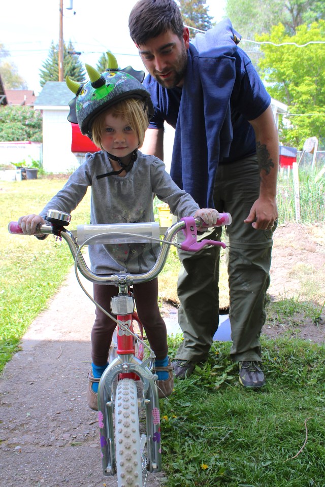 Caleb holding up Lyra on Sammi's bike